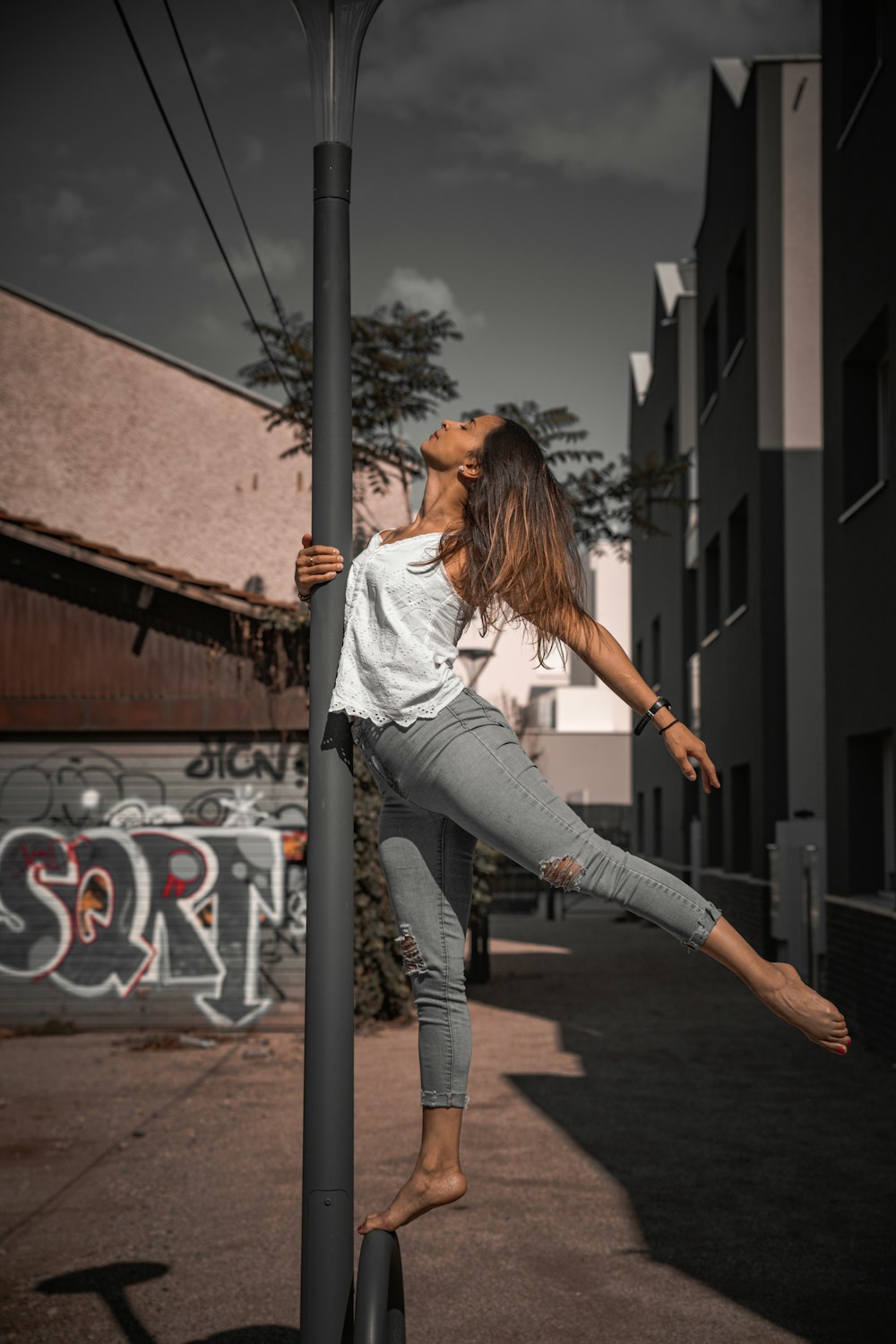 donna in camicia bianca a maniche lunghe e pantaloni grigi in piedi sulla strada di cemento grigia durante il giorno