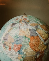 A classic world globe highlighting regions of Africa, Europe, and parts of Asia. The countries are marked with various colors and detailed geographical labels, including borders, cities, and seas. The globe is topped with a metallic pivot point and is set against a neutral background.