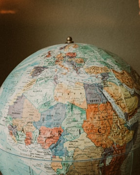 A classic world globe highlighting regions of Africa, Europe, and parts of Asia. The countries are marked with various colors and detailed geographical labels, including borders, cities, and seas. The globe is topped with a metallic pivot point and is set against a neutral background.