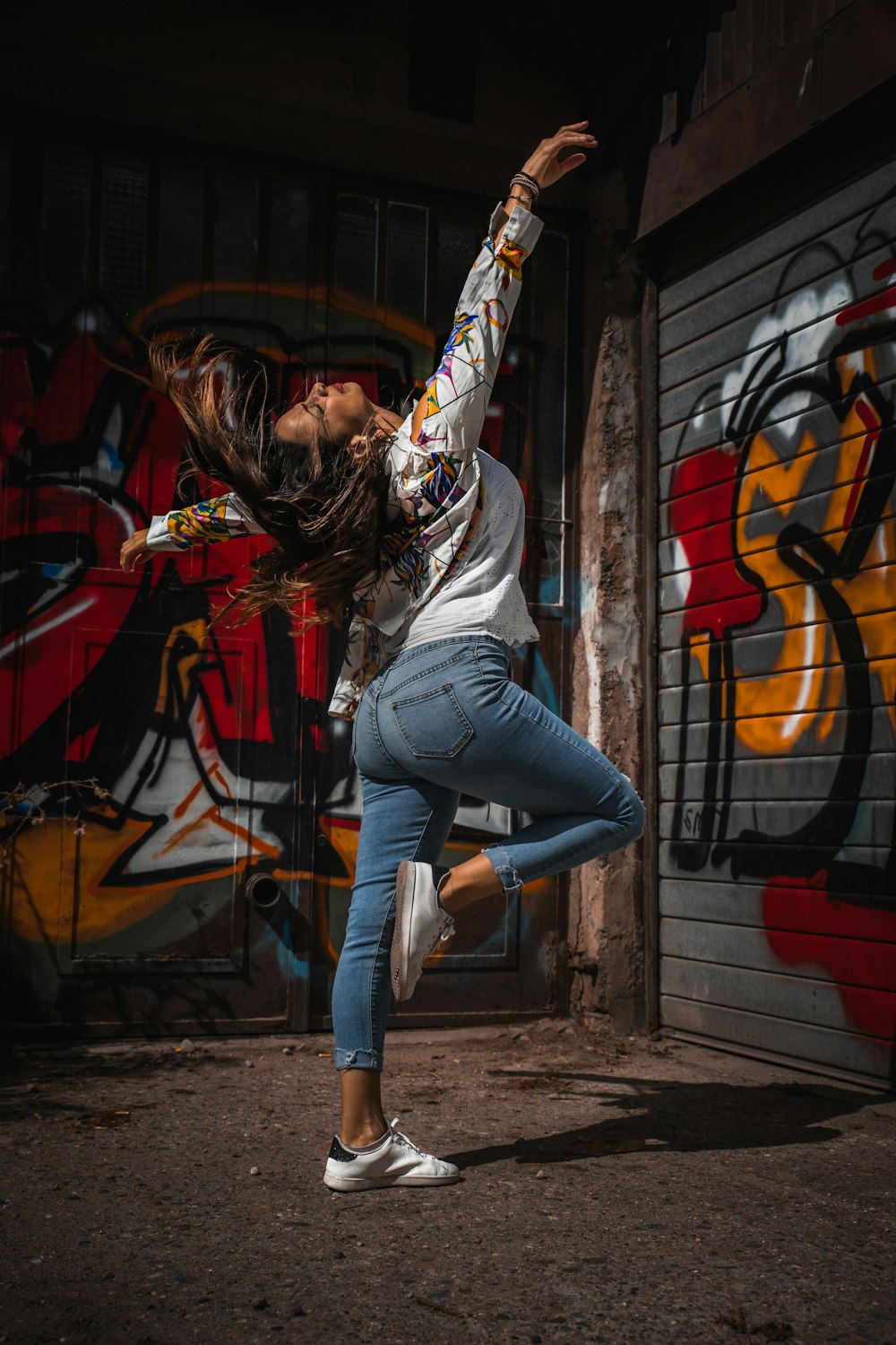 woman in white shirt and blue denim jeans standing beside wall with graffiti