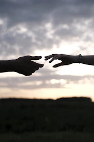 Two hands reaching toward each other in silhouette against a cloudy sky