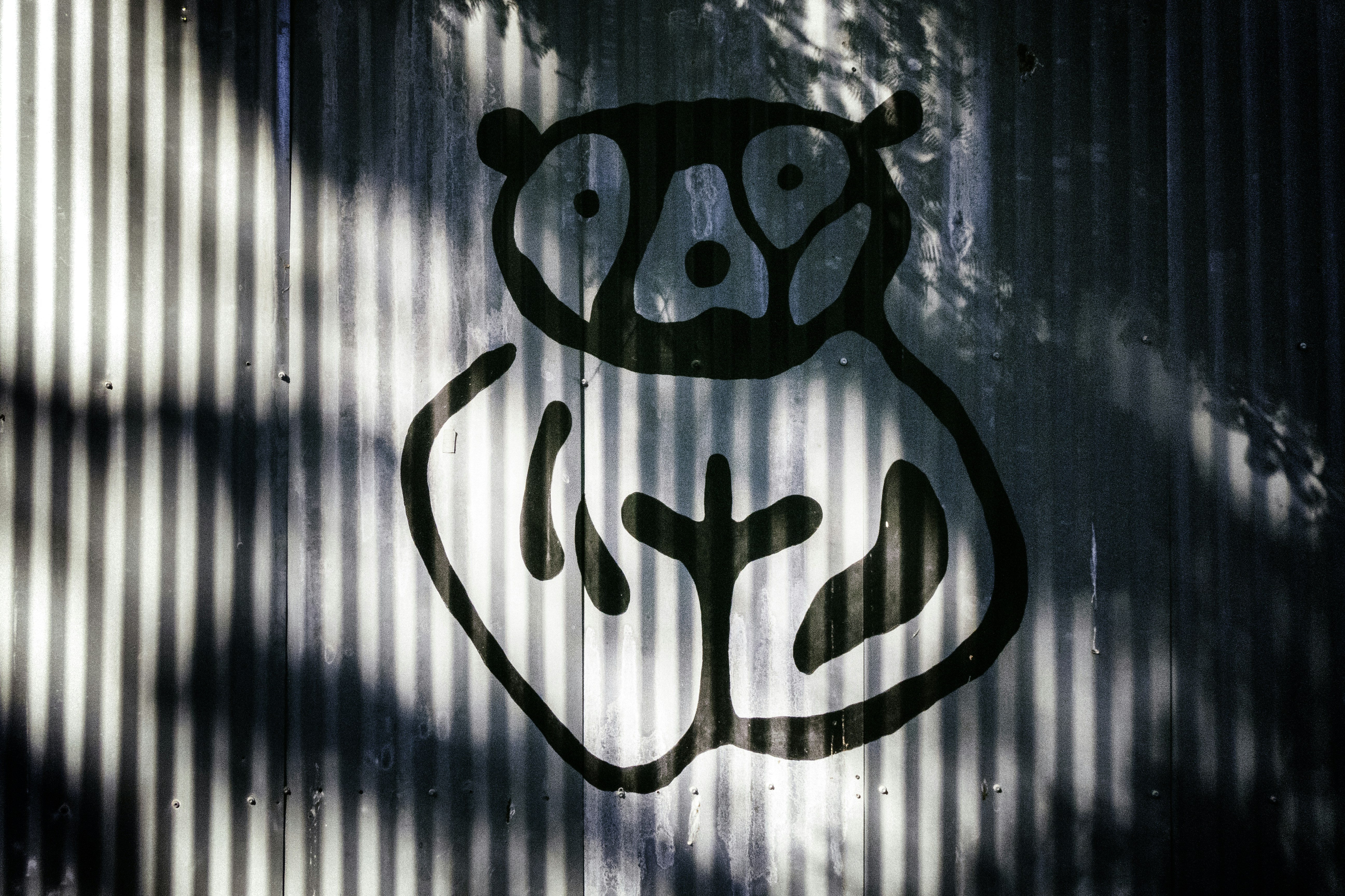 Graffiti panda painted on a corrugated metal wall, with diagonal shadows from foliage creating contrast.