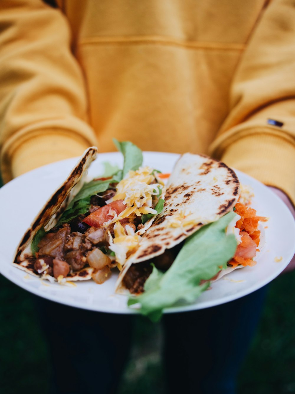 person in brown jacket holding white ceramic plate with food