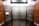 An elevator interior with sleek, metallic doors and wood panel siding. Control panels with buttons and warning signs are situated on either side, with clear labels and numbers. The lighting is bright, accentuating the polished surfaces.
