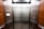An elevator interior with sleek, metallic doors and wood panel siding. Control panels with buttons and warning signs are situated on either side, with clear labels and numbers. The lighting is bright, accentuating the polished surfaces.
