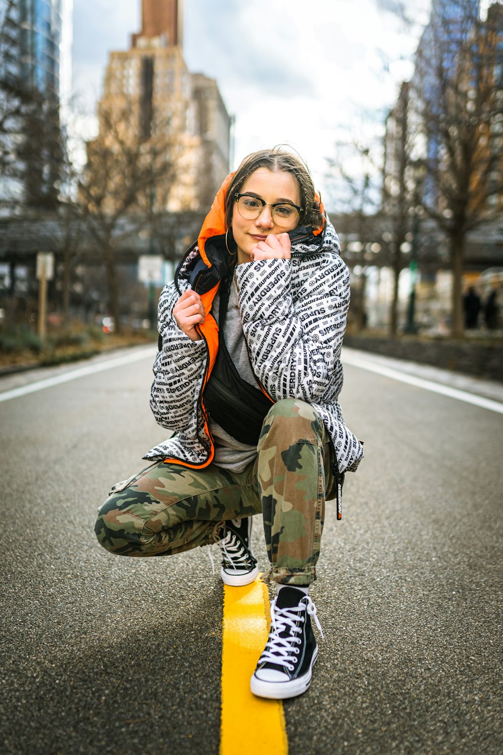 woman in black and white jacket sitting on yellow and black road sign during daytime