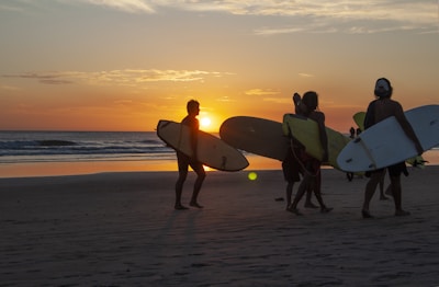 Group of friends laughing and carrying surfboards along the beach.