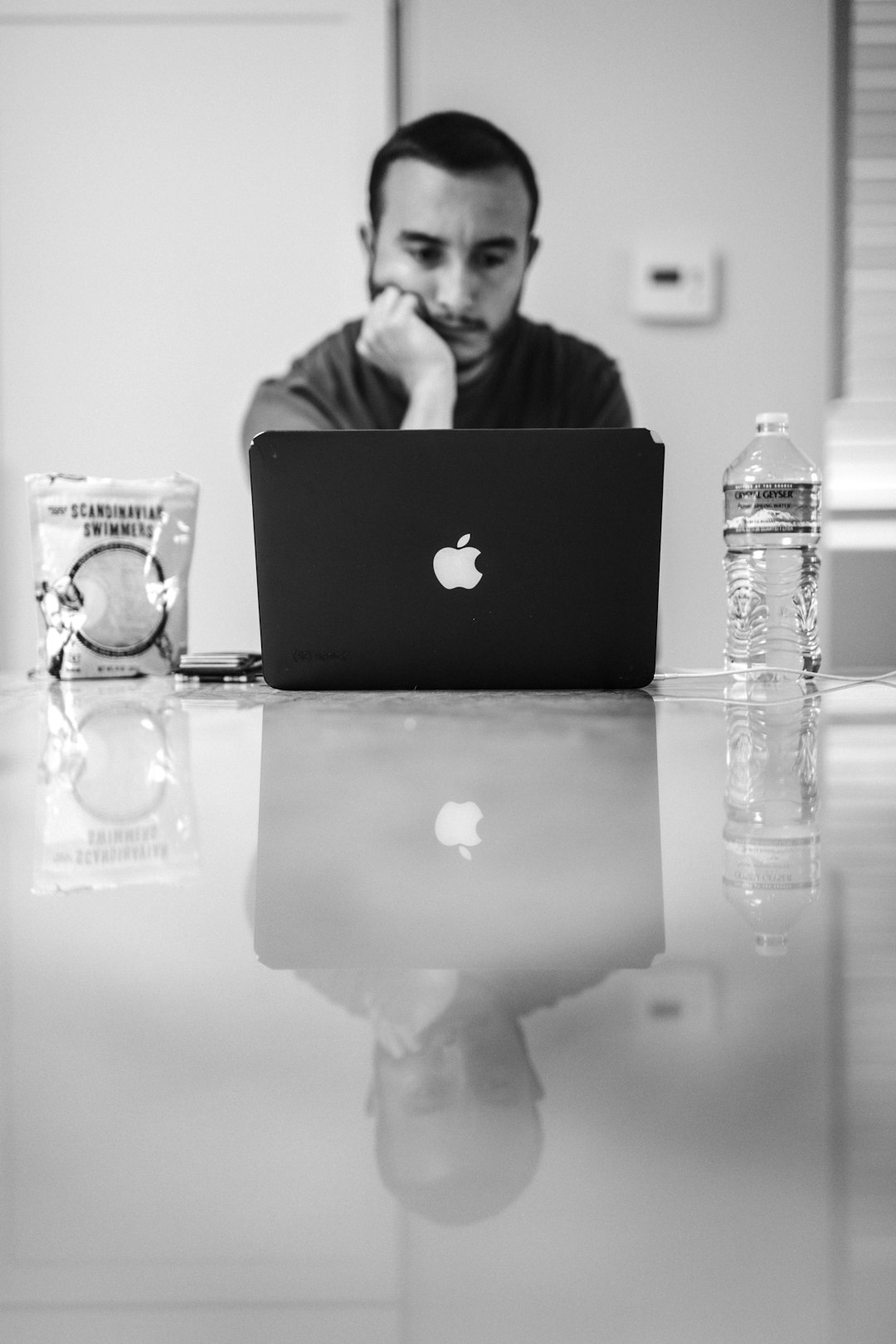 grayscale photo of macbook air beside clear plastic bottle