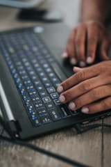 Close-up of hands typing on a laptop with a blue and white theme.