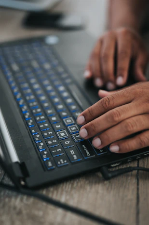 Close-up of hands typing on a laptop keyboard with a blue-themed interface on screen.