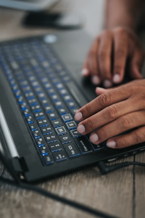 Close-up of hands typing on a laptop with a blue-themed interface on screen.