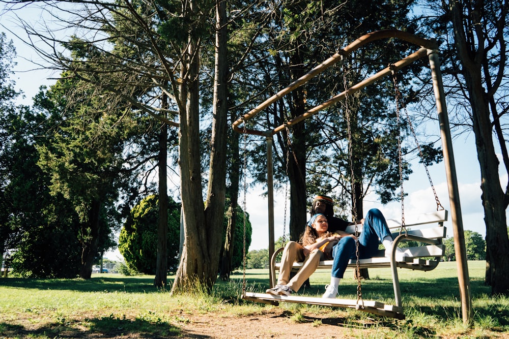 man and woman sitting on swing chair under green leaf trees during daytime