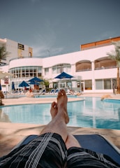 person in black shorts lying on blue and white stripe bed near swimming pool during daytime