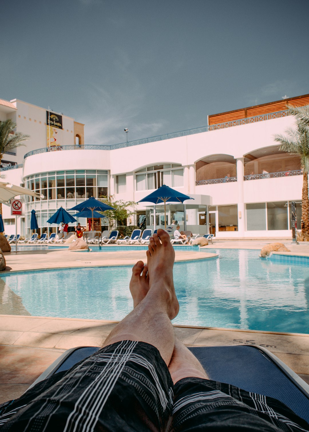 person in black shorts lying on blue and white stripe bed near swimming pool during daytime