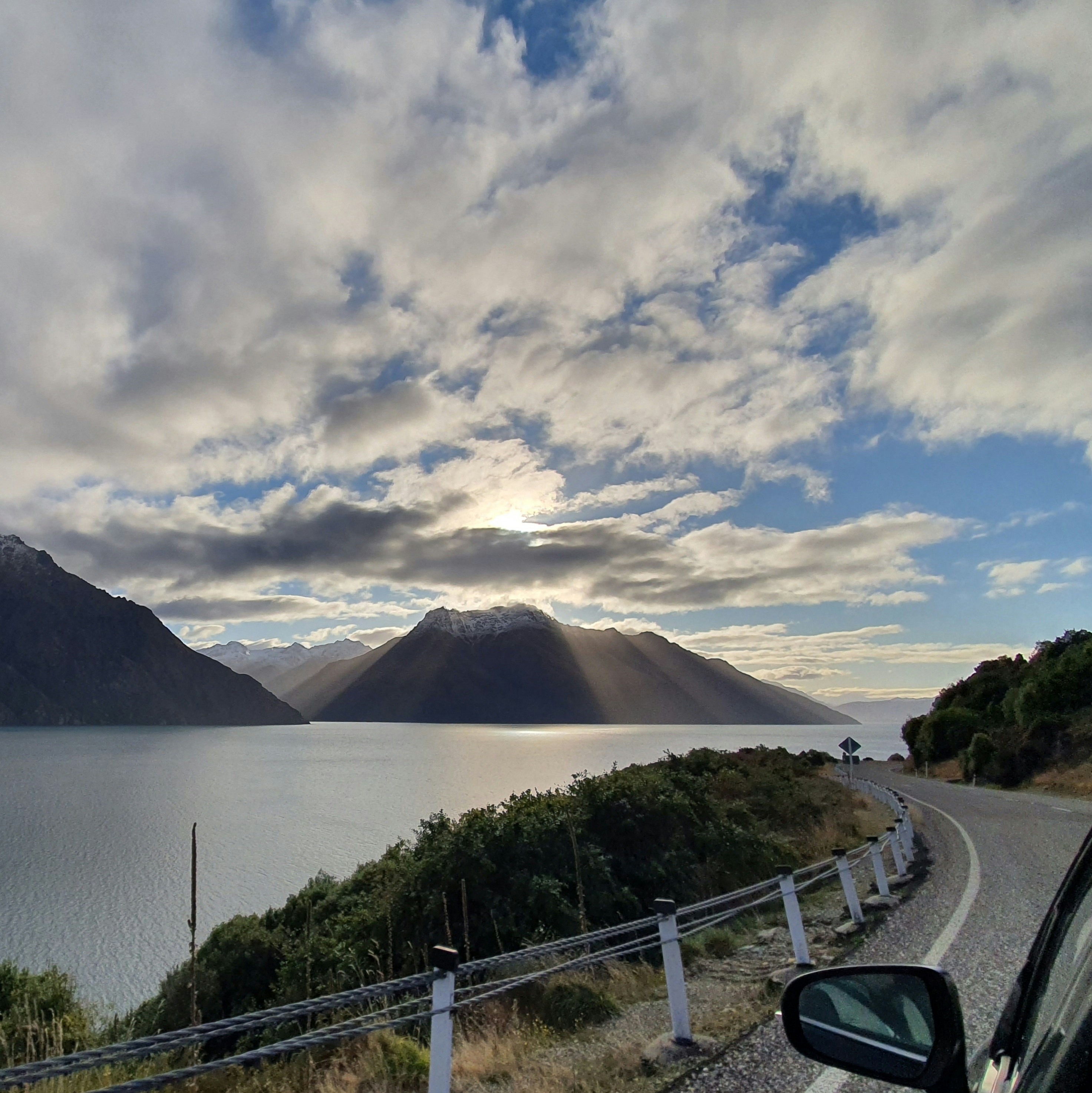 An open road curving alongside a lake beneath New Zealand mountains at sunrise