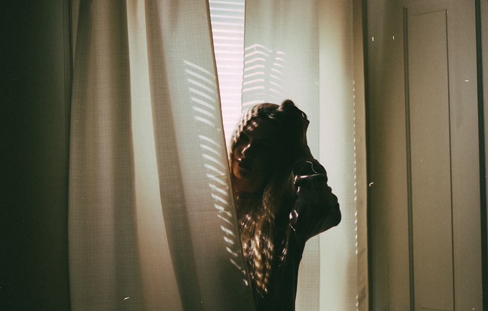 woman in black long sleeve shirt standing near white window curtain