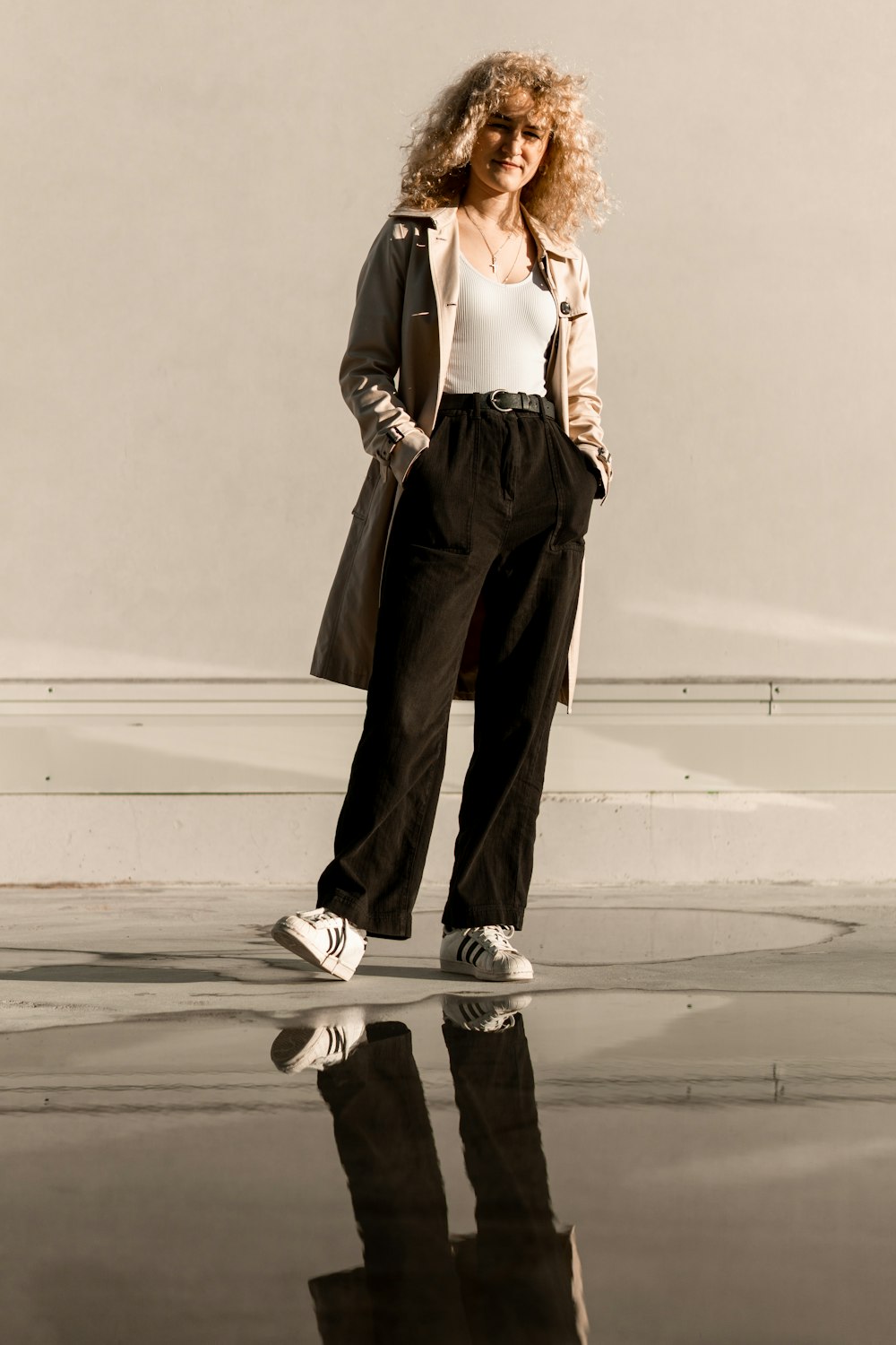 woman in white tank top and brown pants standing on gray sand during daytime