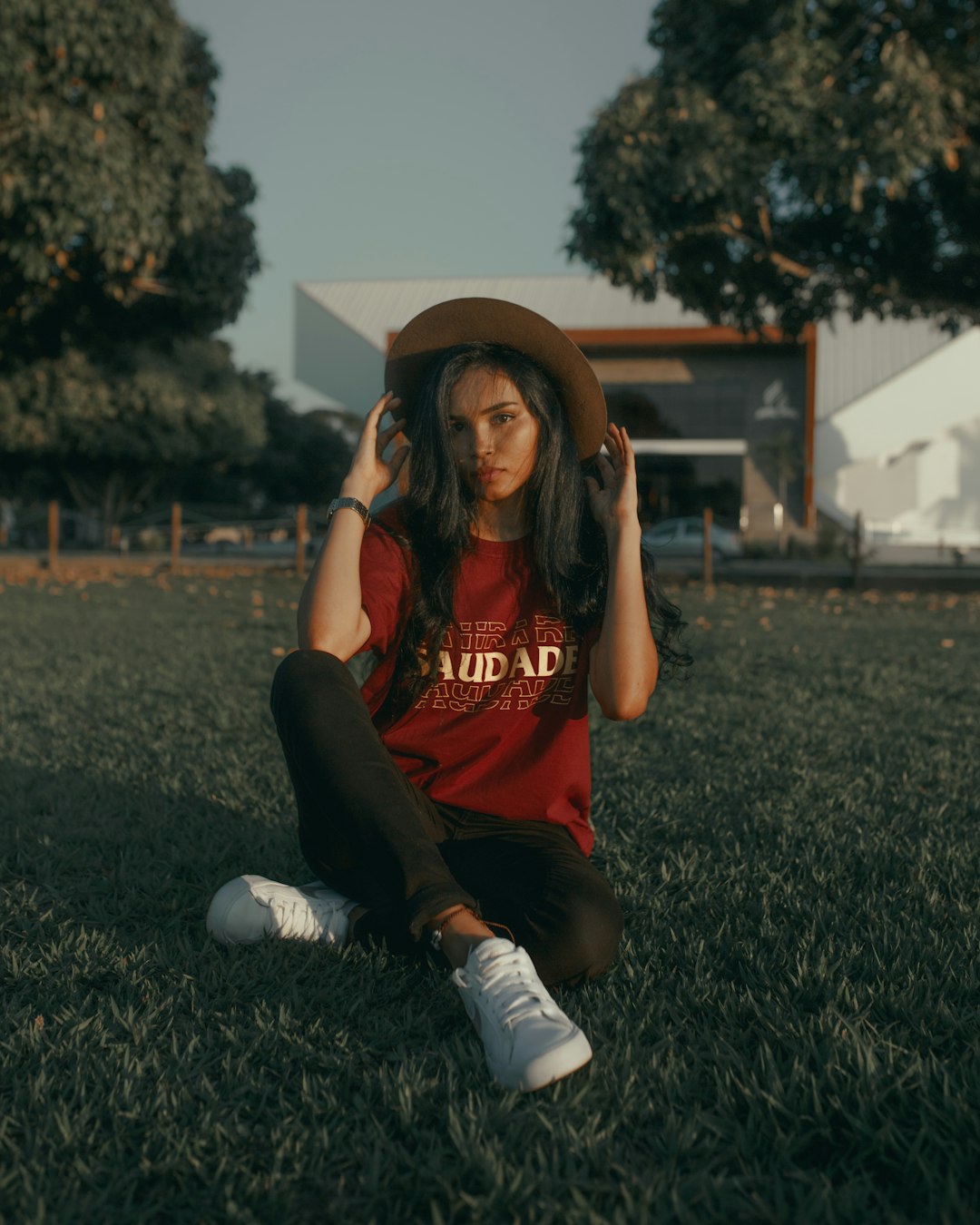 woman in red and white t-shirt and brown fedora hat sitting on green grass field