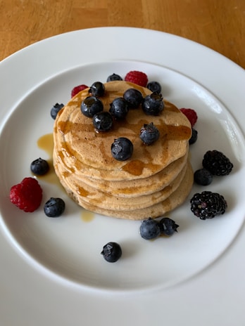 A stack of golden pancakes drizzled with maple syrup and fresh berries on a rustic wooden table.