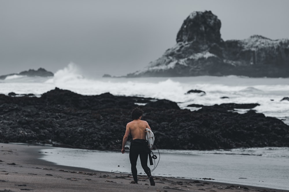 topless man in black pants and black shoes walking on beach shore during daytime