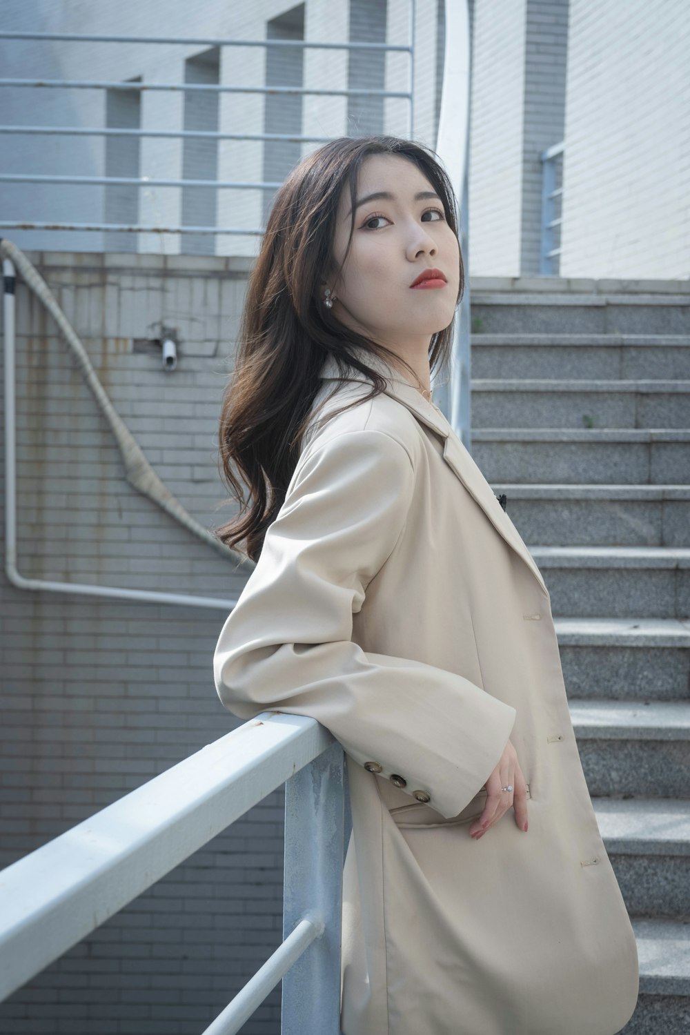 woman in beige coat sitting on white concrete stairs