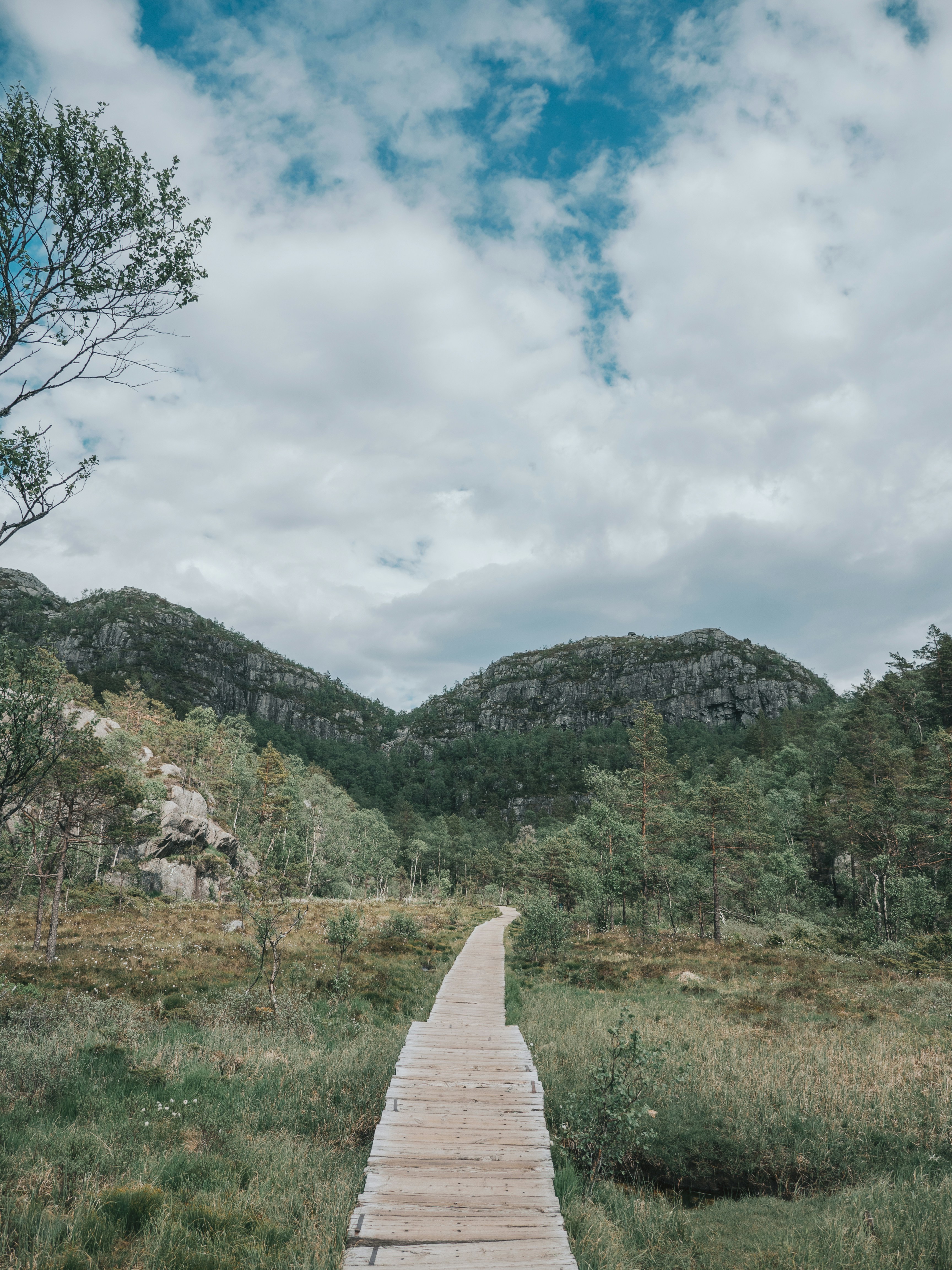 green grass field near mountain under white clouds during daytime