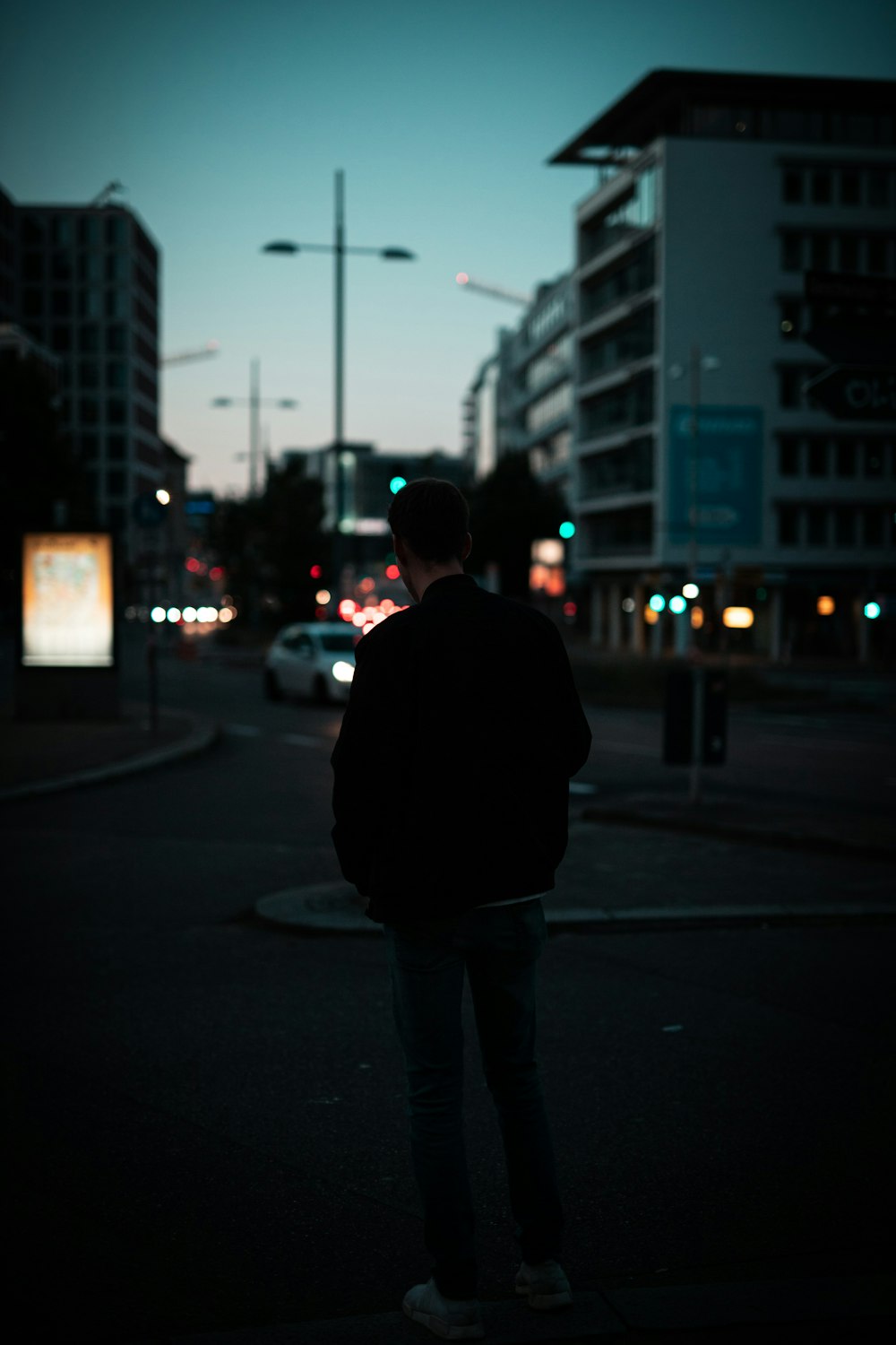 man in black jacket standing on sidewalk during night time