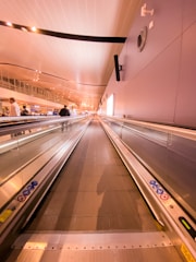 A busy airport terminal featuring a long moving walkway with travelers