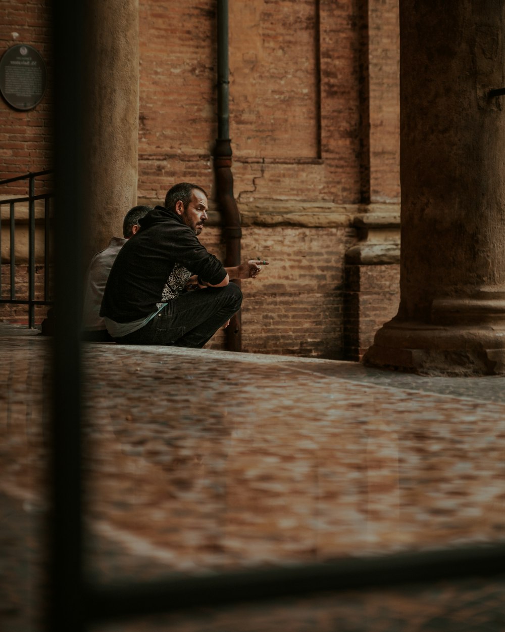 man in black jacket sitting on brown concrete floor