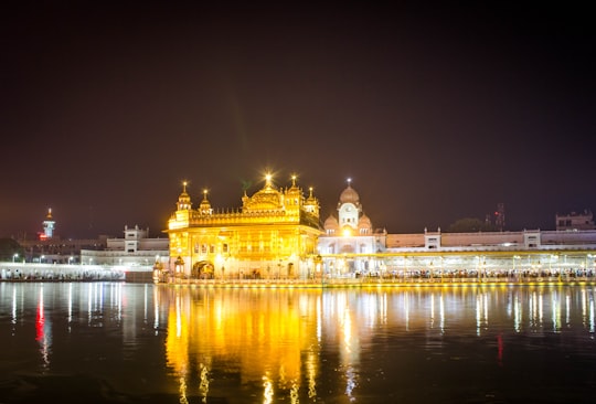 yellow and white concrete building near body of water during nighttime in Harmandir Sahib India