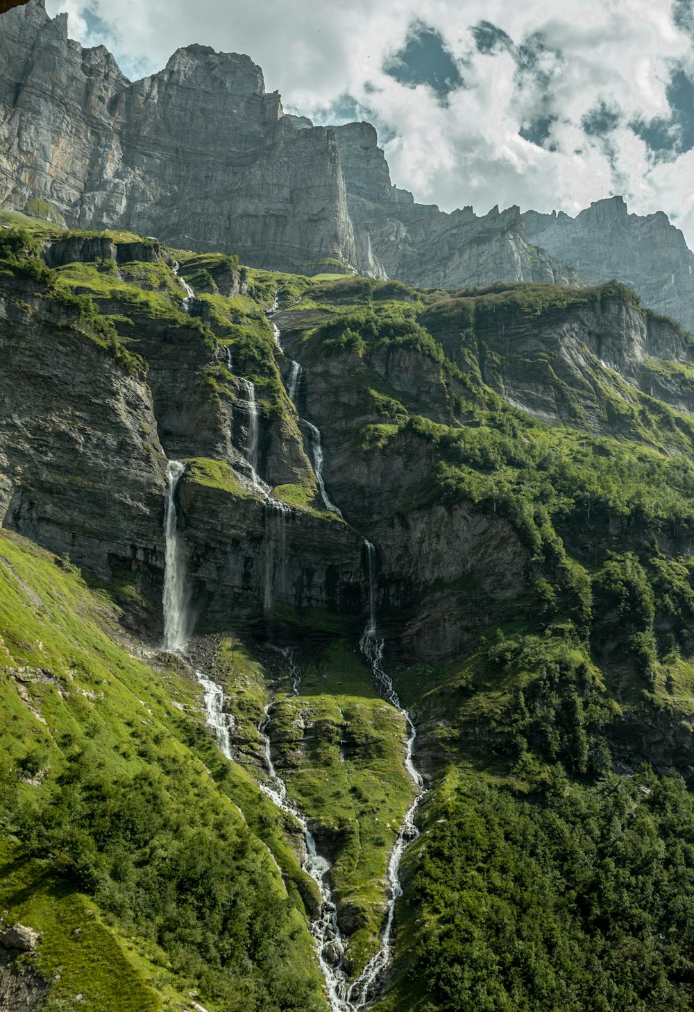 waterfalls on green and gray mountain under white clouds and blue sky during daytime