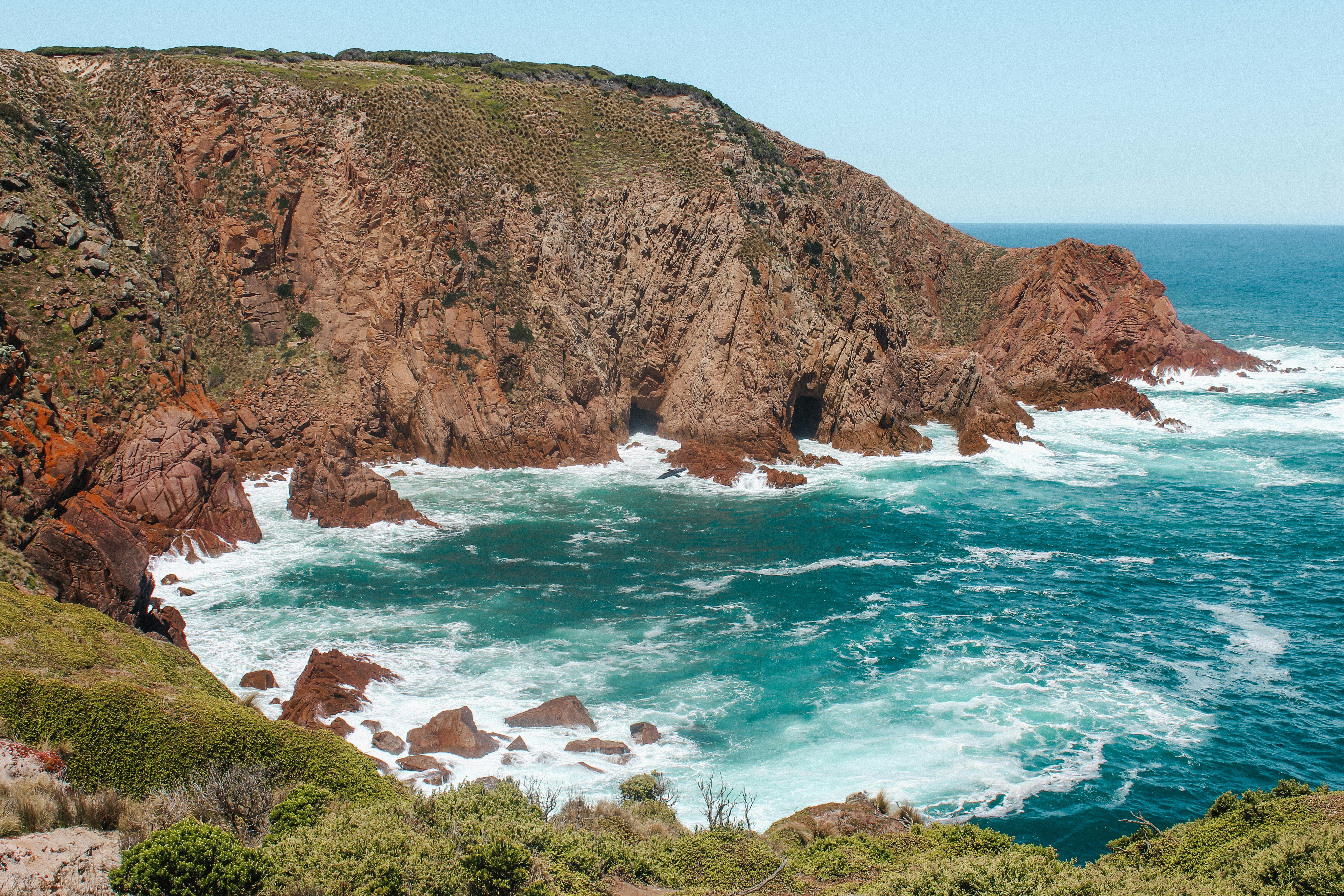 brown rocky mountain beside blue sea during daytime