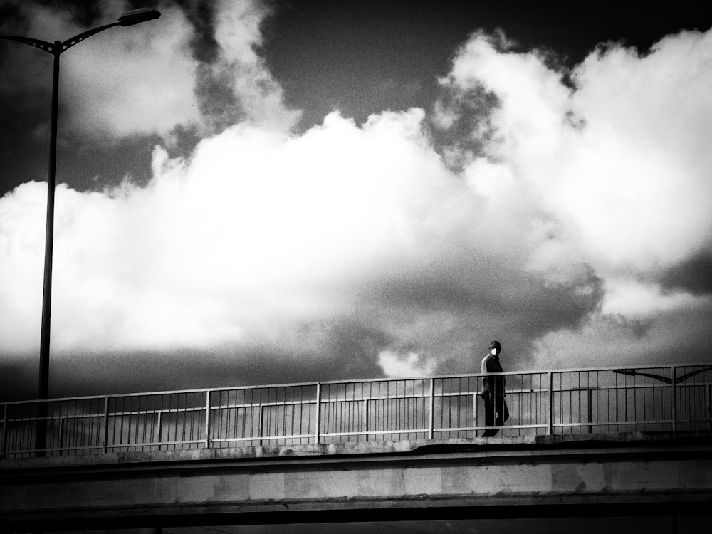 grayscale photo of man standing on bridge