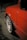 A close-up view of a red car with a focus on its rear fender and a white wheel featuring red text that reads 'OZ Racing'. The car's bodywork shows signs of damage near the wheel arch. The background is dimly lit and out of focus, suggesting nighttime.
