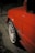 A close-up view of a red car with a focus on its rear fender and a white wheel featuring red text that reads 'OZ Racing'. The car's bodywork shows signs of damage near the wheel arch. The background is dimly lit and out of focus, suggesting nighttime.