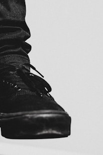 A close-up view of a black sneaker is depicted, highlighting detailed textures and stitching. The shoe is prominently displayed against a minimalistic, light-colored background, creating a stark contrast.
