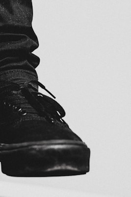 A close-up view of a black sneaker is depicted, highlighting detailed textures and stitching. The shoe is prominently displayed against a minimalistic, light-colored background, creating a stark contrast.