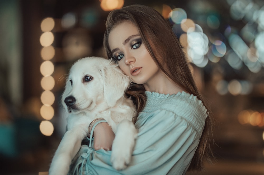 woman in teal long sleeve shirt holding white puppy