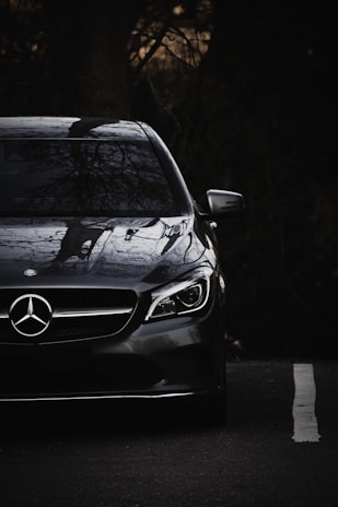 A sleek black Mercedes parked on a dark street with golden streetlights reflecting on its surface.