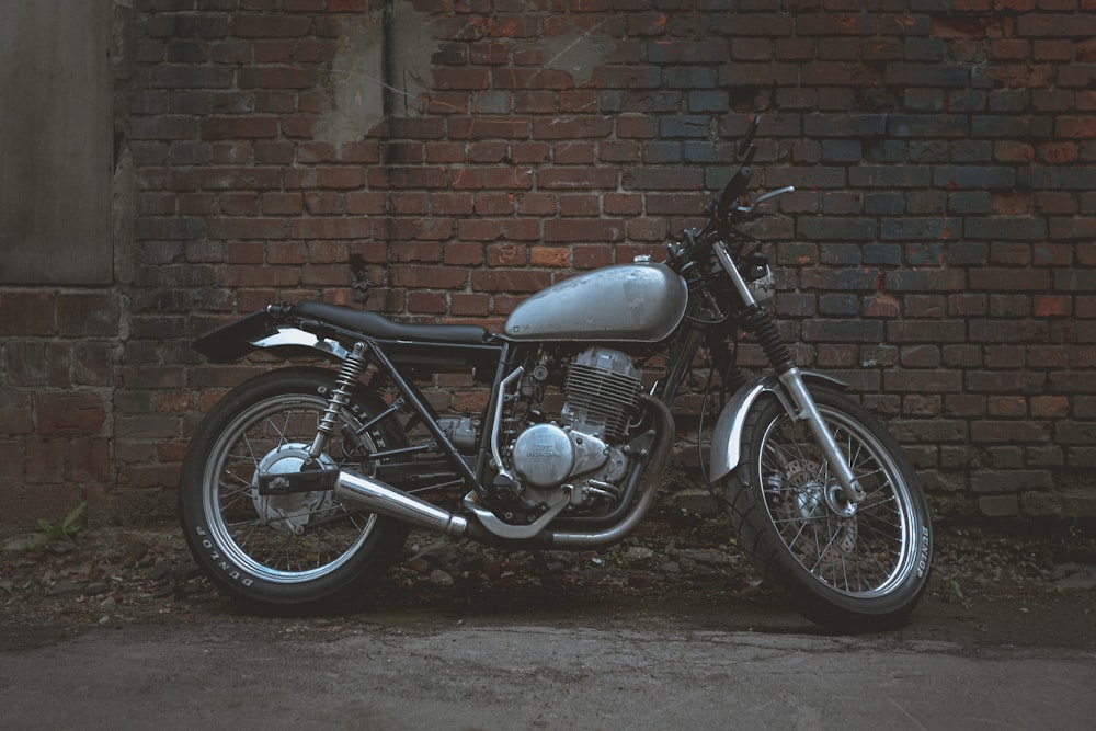 black standard motorcycle parked beside brown brick wall