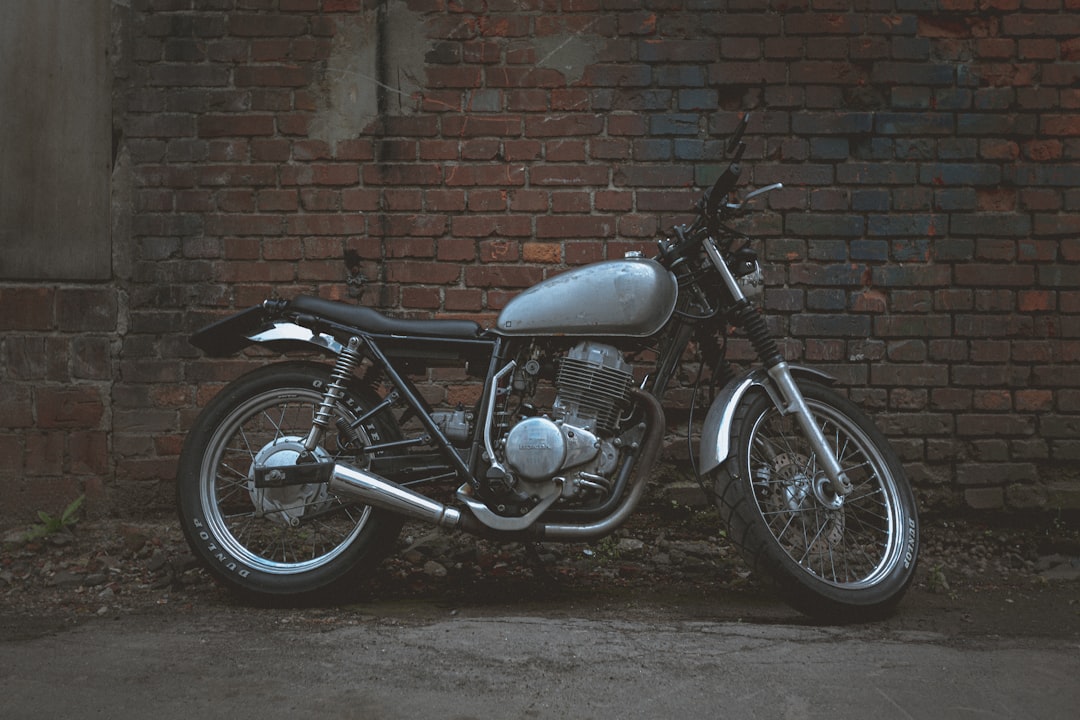 black standard motorcycle parked beside brown brick wall, Vintage bike stands against an old brick wall.