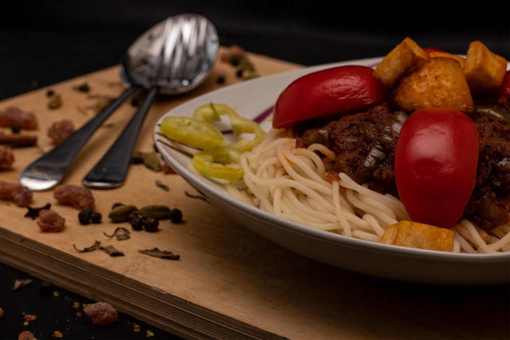 pasta on white ceramic plate beside red tomato on brown wooden table