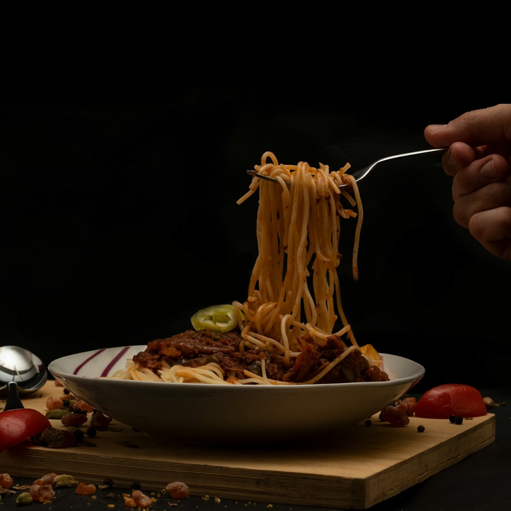 person holding stainless steel spoon and fork eating pasta