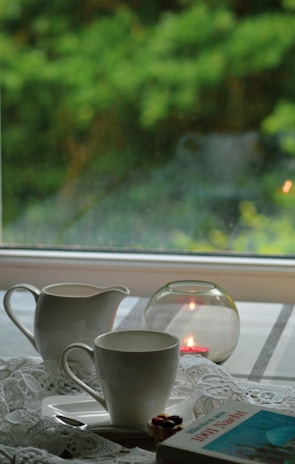 A tranquil morning scene with a minimalist ceramic cup holding fresh herbal tea beside a softly glowing candle on a wooden table.