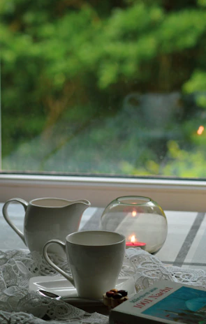 A serene morning scene with a terracotta stoneware cup resting on a wooden table beside a softly flickering candle.