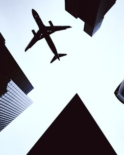 A sleek airplane taking off into a bright blue sky over city skyline.