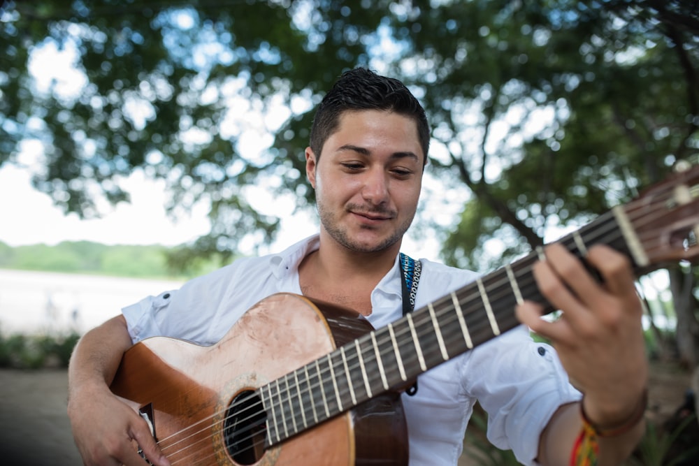 man in white button up shirt playing brown acoustic guitar