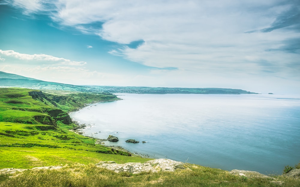 green grass field near body of water under blue sky during daytime