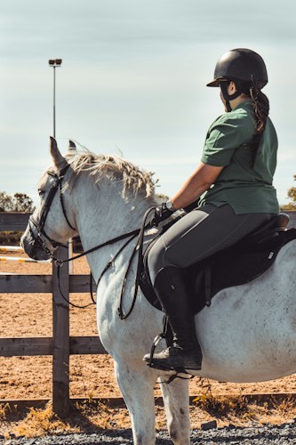 A rider seated on a white horse with an elegant English saddle in a training arena