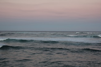 A calm ocean scene with soft waves under a dark blue twilight sky, evoking peace and relaxation.